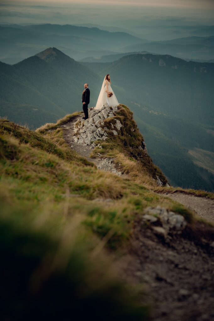 Svadobný pár na vrchole hory s výhľadom na prírodu – romantická svadobná fotografia.